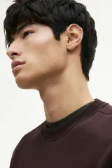 Buzo de cuello redondo color marrón oscuro, confeccionado en tejido de mezcla de algodón con interior cepillado. Presenta un diseño de hombros caídos, corte holgado y terminaciones acanaladas en cuello, puños y bajo.