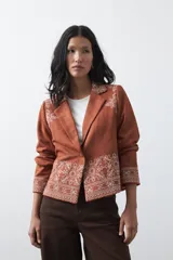 Blazer de gamuza color terracota con bordados decorativos en color crudo en solapas, puños y ruedo. Presenta corte recto, solapas clásicas y cierre frontal con un botón forrado.