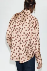 Camisa de corte clásico confeccionada en tela satinada, con estampado de lunares en contraste. Presenta cuello solapa, cierre frontal con botones y mangas largas con puños rectos.