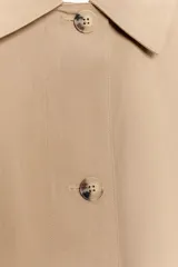 Chaqueta de corte recto y estilo camisero en color beige, con cuello solapa, manga larga y cierre frontal con botones. Presenta dos bolsillos delanteros de plastrón.