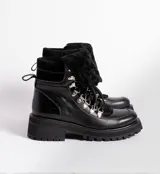 Borcegos de cuero vacuno en tonos marrón, con diseño de caña media y cuello con forro de piel sintética negra. Presentan cordones marrones, ganchos metálicos para ajuste y suela de goma tipo track con plataforma.