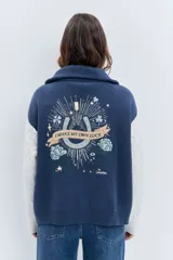 Cardigan de punto con diseño bicolor, cuerpo en color marrón y mangas largas en color crema con textura trenzada. Presenta cuello polo, cierre frontal con cremallera y puños acanalados.