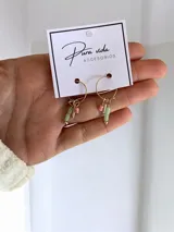 Aros tipo argolla dorados con dijes colgantes de cuentas cilíndricas en tonos verde pastel y rosado.