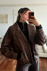 Campera bomber de cuero ovino en tono óxido, con diseño de solapas, cierre frontal con botones de guampa y detalles de pasamanería trenzada en las mangas.