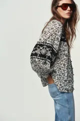 Blusa blanca con estampado floral en negro, cuello redondo con escote pico y manga larga abullonada. Presenta bordados y abalorios en el escote y los puños. Cierre frontal con botones.