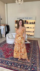 Vestido largo naranja con estampado floral de estilo setentero, escote en V profundo y tirantes finos.