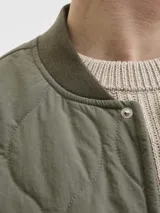 Chaleco acolchado color verde oliva, con diseño de matelassé, cuello estilo baseball y cierre frontal con botones a presión. Cuenta con dos bolsillos frontales y un bolsillo pequeño en el pecho con etiqueta de marca.