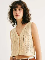 Chaleco de punto calado en color beige, con escote en V y cierre frontal con botones. Presenta un diseño sin mangas y corte recto.