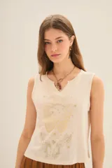 Musculosa color crema con estampado de mariposa y manos en dorado, escote en V con tachas y corte holgado.