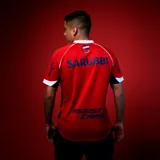 Camiseta de fútbol Umbro del Club Nacional de Football, modelo Away 2025. Diseño en color rojo con detalles en azul y blanco en el cuello y los puños. Incluye el escudo del club, el logo de Umbro y los patrocinadores estampados en el frente y las mangas.