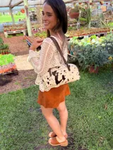 Cartera baguette de cuero color crudo con manchas negras, forro interno de tela y correa de cuero marrón.