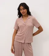 Pijama largo de dos piezas confeccionado en ribana con estampado de cuadros vichy en tonos marrón y blanco. Incluye una blusa de manga corta con cuello solapa, cierre frontal de botones y detalles de vivo contrastante, y un pantalón de pierna recta con cintura elástica.