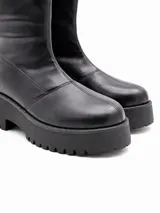 Bota de caña alta color negro, con suela track de plataforma y taco cuadrado. Diseño minimalista con costuras visibles en la puntera.