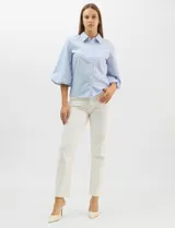 Camisa de algodón con patrón de rayas verticales, cuello camisero clásico y cierre frontal con botones. Presenta detalles metálicos aplicados en el frente y mangas, con mangas 3/4 abullonadas y ruedo recto.