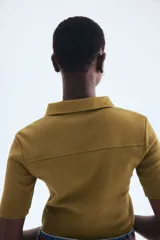 Top de punto color verde oliva, ajustado al cuerpo, con cuello camisero, tapeta de botones y costuras decorativas verticales en el frente.