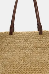 Bolso tipo shopper confeccionado en yute trenzado, con doble asa de mano en cuero sintético color marrón.