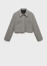Chaqueta corta de diseño recto y estilo sastrero, confeccionada en tejido fluido color gris. Presenta cuello camisero, cierre frontal con botones ocultos y dos bolsillos de parche en el frente.