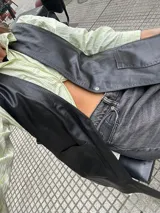 Chaleco de cuero negro, abierto a los costados, con tiras que se regulan a necesidad y gusto de cada una. Presenta bolsillos frontales y escote en V.