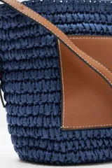 Bolso bandolera azul tejido con bolsillo de cuero marrón en el frente y correa larga de cuero marrón.