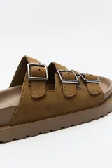 Sandalia negra tipo slide con plataforma gruesa y tres tiras ajustables con hebillas metálicas plateadas. La capellada es de material con textura de gamuza o nobuck.