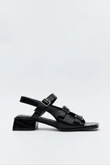 Sandalia negra de cuero sintético con textura símil reptil, taco medio cuadrado y múltiples tiras con hebillas metálicas ajustables.