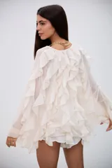 Blusa color crudo con volados en el frente y en las mangas largas, confeccionada en tela semitransparente con cierre frontal de botones.