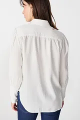 Camisa de color marrón claro, con cuello clásico, cierre frontal de botones y mangas largas con puños ajustados y volumen en los hombros.