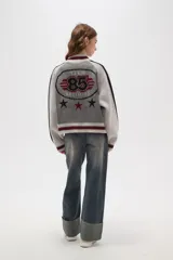 Campera de punto con cierre frontal, cuello alto y diseño de rayas laterales en mangas. Presenta un patrón texturizado en el cuerpo y detalles de rib acanalado en puños, cuello y ruedo.