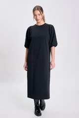 Vestido negro de corte recto y largo midi, con cuello redondo y mangas globo cortas. Presenta pespuntes contrastantes en color claro que recorren el frente y los hombros.