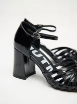 Sandalias de taco alto ancho con diseño retro, confeccionadas en charol negro. Presentan tiras delanteras múltiples entrelazadas, talón cerrado y una correa fina ajustable al tobillo con hebilla metálica.