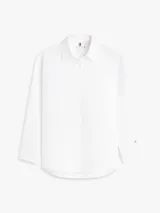 Camisa blanca de algodón orgánico con cuello camisero, cierre frontal de botones y manga larga ajustable con presilla. Cuenta con el logo de Tommy Hilfiger bordado sutilmente en el pecho.