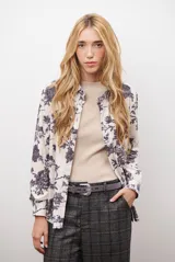 Camisa de manga larga con cuello clásico y cierre frontal de botones. Presenta un estampado floral en tonos marrones sobre una base color beige, confeccionada en un tejido con textura similar al gamuzado.