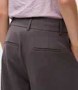 Pantalón de sastrería modelo barrel, de tiro alto y corte amplio con piernas anchas. Presenta pliegues frontales, trabillas para cinturón y recortes decorativos en la parte delantera.