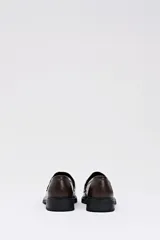 Mocasín de estilo clásico en color chocolate, confeccionado en cuero sintético liso con detalle de empeine en pelo sintético con estampado de manchas de vaca.