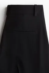 Pantalón sastrero negro de corte amplio con pinzas, cierre oculto, bolsillos al bies y bolsillos decorativos traseros.