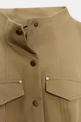 Blazer entallada color beige con cuello subido, manga larga con hombreras y trabillas en los hombros. Presenta bolsillos de plastrón en el delantero, detalle de solapas en el pecho y cierre frontal con botones a presión.
