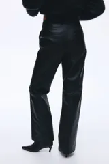 Pantalón de cuero sintético negro con corte bootcut, cierre frontal con botón oculto y costuras decorativas sobre las rodillas.