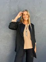 Chaqueta negra de corte recto y largo medio, con cuello redondo sin solapas y mangas largas con vuelta en color beige en los puños.