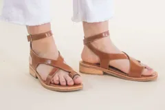 Sandalias de cuero color marrón con tiras cruzadas y tobillera con hebilla.
