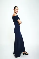 Vestido largo de punto color azul marino, con escote recto tipo off-shoulder con detalle de frunces en la parte superior. Presenta un diseño entallado en el torso y una falda con caída fluida y bajo combinado en tejido semitransparente.