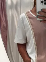 Remera de diseño combinado en algodón y lino, con panel frontal y posterior en color amarillo suave y laterales en blanco. Presenta detalles de puntilla vertical en la unión de los paneles, cuello redondo y un corte asimétrico con el ruedo trasero ligeramente más largo.