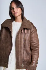 Campera gamulán marrón de símil cuero, con interior de corderoy al tono, cierre frontal con cremallera y cuello con solapas grandes. Presenta detalles de hebillas en los puños y bolsillos laterales con cierre.