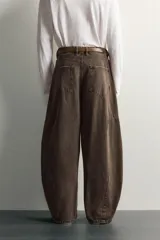 Pantalón barrel fit de mezclilla color verde militar, con efecto lavado, cinco bolsillos, cierre frontal con cremallera y botón, y detalle de pinzas en las rodillas.