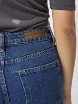 Jean de corte recto y tiro medio, con diseño clásico de cinco bolsillos. Presenta un lavado azul medio y terminación de ruedo desflecado.