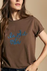 Remera de manga corta color marrón, con la frase "la dolce vita" bordada en azul en el frente y mangas con dobladillo.