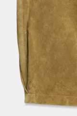 Pantalón de piel color tostado, tiro medio con cierre frontal de cremallera y botón, bolsillos delanteros y traseros, y bajo con acabado de pliegues.