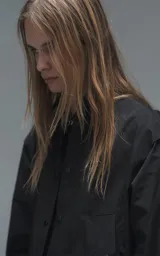 Chaqueta tipo overshirt de microfibra, color negro, con calce oversize y ruedo curvo. Presenta cierre frontal con broches a presión, bolsillos frontales de gran tamaño y cierres laterales a lo largo de las mangas para ajustar su amplitud.