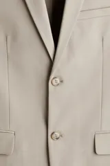 Blazer color beige de corte slim fit, con solapas de muesca finas, ojal decorativo, botonadura sencilla, bolsillo superior insertado, bolsillos delanteros con solapa, dos bolsillos interiores, botones decorativos en los puños y abertura doble en la parte posterior.