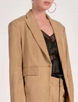 Blazer de mujer color beige, confeccionado en material similar a la gamuza, con solapas anchas, un botón forrado en la parte frontal y bolsillos de ojal.