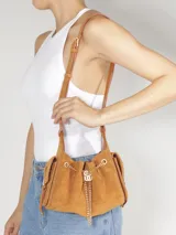 Cartera bucket mini de gamuza marrón tostado, modelo de Schutz con correa ajustable para el hombro y detalles de cadena dorada con dije frontal.